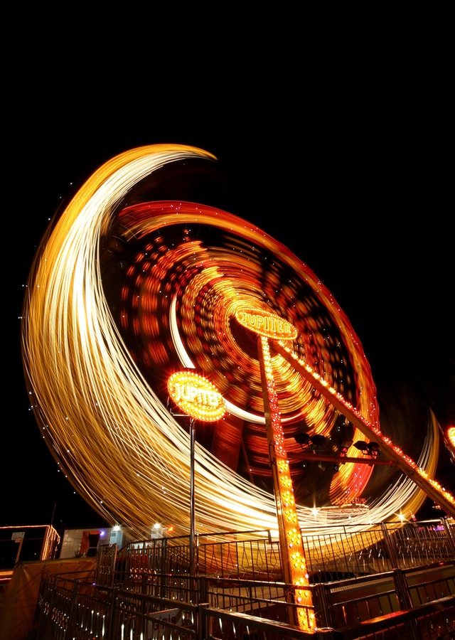 Time-elapse photo of a ferris wheel at night, showing arcs of white, yellow, orange and red light against a dark sky. Photo by Engin Akyurt via Pexels.