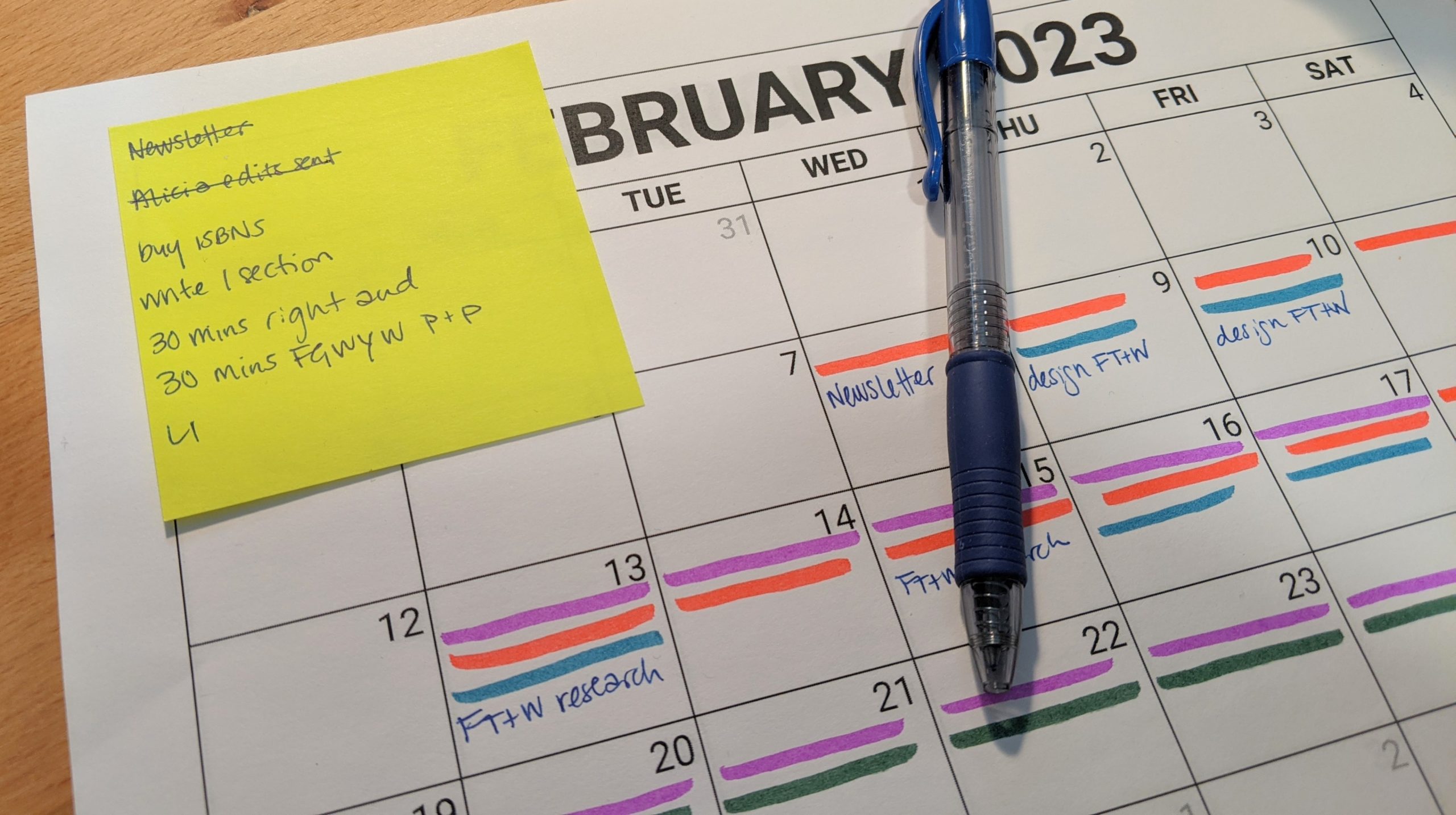 A neon yellow post-it with a short to-do list in blue ink and a blue pen over a printed calendar sheet.